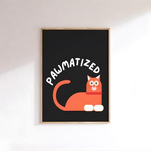 Puede incluir: Un cuadro enmarcado con un gato de dibujos animados naranja, patas blancas y un collar rojo, sobre un fondo negro. La palabra "PAWMATIZED" está escrita en blanco sobre el gato. La obra de arte está en un marco de madera.