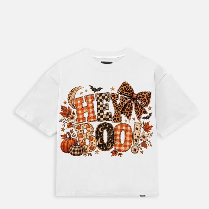 K&ouml;nnte beinhalten: Ein wei&szlig;es Kurzarm-T-Shirt mit einem Grafikdruck, der HEY BOO in gemusterten Buchstaben zeigt. Das Design enth&auml;lt orangefarbene Karomuster, schwarz-wei&szlig; karierte und Leopardenmuster-Texturen, akzentuiert mit K&uuml;rbissen, Bl&auml;ttern und einer Schleife.