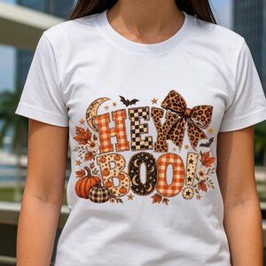 K&ouml;nnte beinhalten: Ein wei&szlig;es Kurzarm-T-Shirt mit einem Grafikdruck, der in gro&szlig;en Buchstaben HEY BOO zeigt. Das Design umfasst eine Schleife mit Leopardenmuster, orangefarbenes Karomuster, schwarz-wei&szlig;es Schachbrettmuster, K&uuml;rbisse, Herbstbl&auml;tter und Flederm&auml;use.