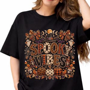 Könnte beinhalten: Ein schwarzes T-Shirt mit einem Grafikdruck, der den Text SPOOKY VIBES in Leoparden- und Karomustern zeigt. Das Design umfasst einen Hexenhut, Schleifen, Geister, Totenköpfe, Kürbisse, Spinnennetze und Fledermäuse in orangefarbenen, schwarzen und weißen Tönen.