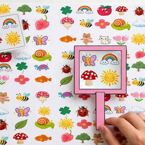Puede incluir: Una hoja de papel blanca cubierta con pegatinas de dibujos animados coloridos que incluyen abejas, arcoíris, setas, soles, mariposas, caracoles, mariquitas, flores y nubes. Una tarjeta cuadrada y un marco de lupa rosa muestran conjuntos.