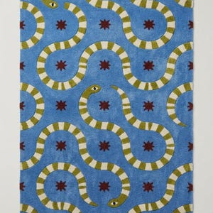 May include: A rectangular area rug featuring a bright blue background with a repeating pattern of winding snakes in olive green and cream stripes, interspersed with small, dark red eight-pointed star shapes across the entire surface.