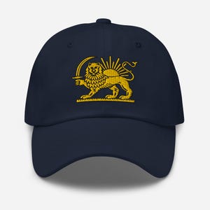 Op de afbeelding: Marineblauwe baseballcap met een goud geborduurd embleem van een leeuw met een zwaard, met een opkomende zon erachter. De cap heeft een gebogen klep en een verstelbare band. Een modieus accessoire.
