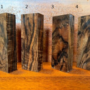 May include: Four rectangular wooden blocks arranged in a row, labeled with the numbers 1, 2, 3, and 4. Each block features a distinct grain pattern with swirling dark brown and black streaks against a lighter tan and golden brown wood base.