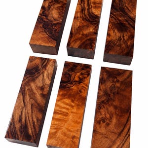 May include: Six rectangular wooden blocks arranged in two rows of three. Each block features a distinct, rich brown wood grain pattern with swirling dark brown and amber tones, showcasing a smooth, polished surface and sharp, clean edges.