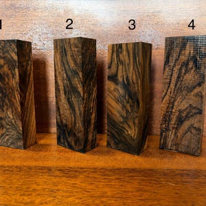Può includere: Quattro blocchi di legno rettangolari etichettati 1, 2, 3 e 4. Ogni blocco presenta un distinto motivo a venature vorticose marrone scuro e nero. I blocchi sono disposti in fila, in posizione verticale, mostrando una finitura lucida con texture del legno naturale.