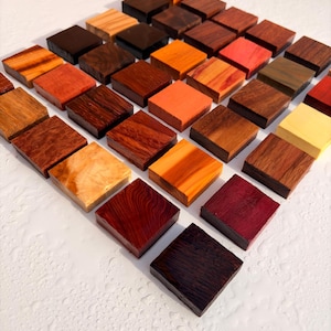 May include: A collection of small, square wooden blocks arranged in a grid pattern. The blocks display a variety of natural wood grains, textures, and colours, ranging from light cream and yellow to deep red, orange, brown, and dark espresso tones.