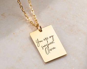 May include: A gold-toned rectangular pendant necklace featuring a delicate chain and a flat metal tag engraved with the cursive script text "You are my sunshine, Olivia." The pendant hangs from a simple jump ring attached to the chain.
