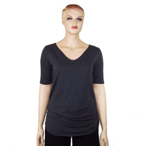 May include: A dark gray V-neck top with short sleeves. The shirt has a ruched detail on the side and is displayed on a mannequin. The top is a solid color and appears to be made of a soft, comfortable material.