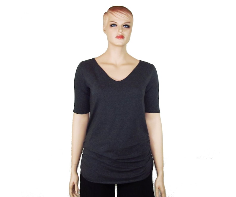 May include: A dark gray V-neck top with short sleeves. The shirt has a ruched detail on the side and is displayed on a mannequin. The top is a solid color and appears to be made of a soft, comfortable material.