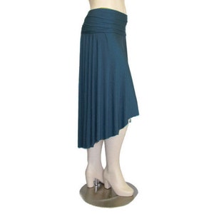 May include: A teal-colored asymmetrical skirt with a wide, ruched waistband. The skirt drapes down to an uneven hemline, creating a flowing silhouette. The fabric appears to be a soft, lightweight material.