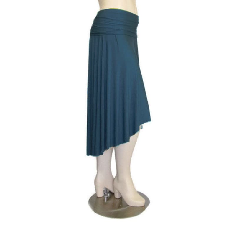May include: A teal-colored asymmetrical skirt with a wide, ruched waistband. The skirt drapes down to an uneven hemline, creating a flowing silhouette. The fabric appears to be a soft, lightweight material.