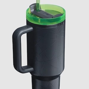 Puede incluir: Vaso t&eacute;rmico negro con tapa y pajita verdes. El vaso tiene un asa y un dise&ntilde;o texturizado de telara&ntilde;a. La tapa es verde y tiene un cierre deslizante. La pajita tambi&eacute;n es verde.
