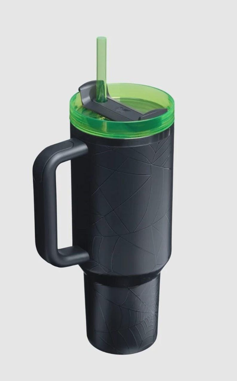 Puede incluir: Vaso t&eacute;rmico negro con tapa y pajita verdes. El vaso tiene un asa y un dise&ntilde;o texturizado de telara&ntilde;a. La tapa es verde y tiene un cierre deslizante. La pajita tambi&eacute;n es verde.