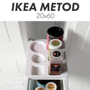 Puede incluir: Una taza de cerámica blanca con asa negra y el texto "But First, Coffee" en negrita negra. La taza se encuentra sobre un fondo borroso, resaltando su diseño limpio.