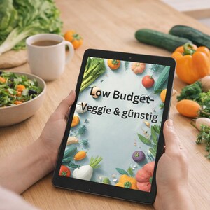 Peut inclure: Une tablette noire affichant un graphique numérique avec le texte Low Budget- Veggie & günstig entouré d'illustrations de divers légumes, dont des tomates, des poivrons et des légumes verts sur un fond bleu clair, tenue verticalement.