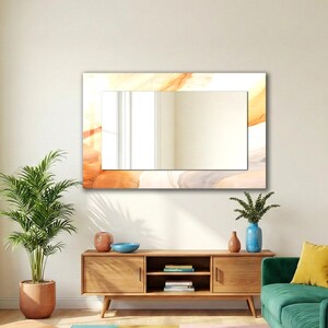 Op de afbeelding: Een rechthoekige wandspiegel met een brede lijst voorzien van een abstract marmerpatroon in tinten oranje, cr&egrave;me en grijs. Het centrale reflecterende glasoppervlak is helder en glad en biedt een scherpe reflectie van de ruimte.