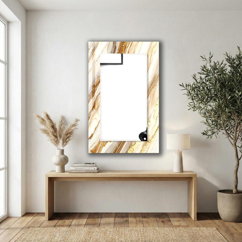 Peut inclure: Un miroir rectangulaire avec un motif marbr&eacute; dans les tons or, blanc et marron. Le miroir est dot&eacute; d'une pince noire en haut et d'un bouton noir en bas. Il est accroch&eacute; &agrave; un mur blanc.