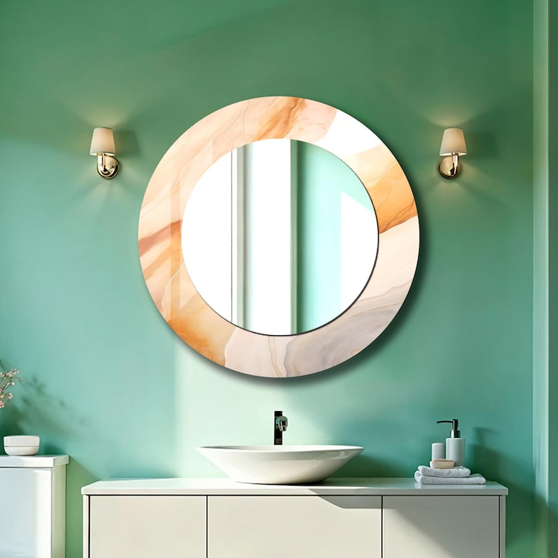 Op de afbeelding: Een ronde wandspiegel met een brede rand voorzien van een wervelend, gemarmerd patroon in tinten van zacht perzik, cr&egrave;me en lichtgrijs. De spiegel heeft een glad, reflecterend middengedeelte en is bevestigd aan een vlakke muur.