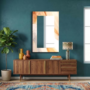 Op de afbeelding: Een rechthoekige wandspiegel met een decoratieve rand met een vloeiend, abstract marmerpatroon in tinten oranje, cr&egrave;me en grijs. Het centrale reflecterende glasoppervlak is helder en glad, omlijst door het gedrukte ontwerp op het glas.
