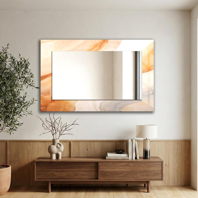 Op de afbeelding: Een rechthoekige wandspiegel met een brede, decoratieve rand met een wervelend, gemarmerd patroon in zachte tinten oranje, perzik en cr&egrave;me. Het centrale reflecterende glasoppervlak is helder en glad, omlijst door het kleurrijke, abstracte ontwerp.