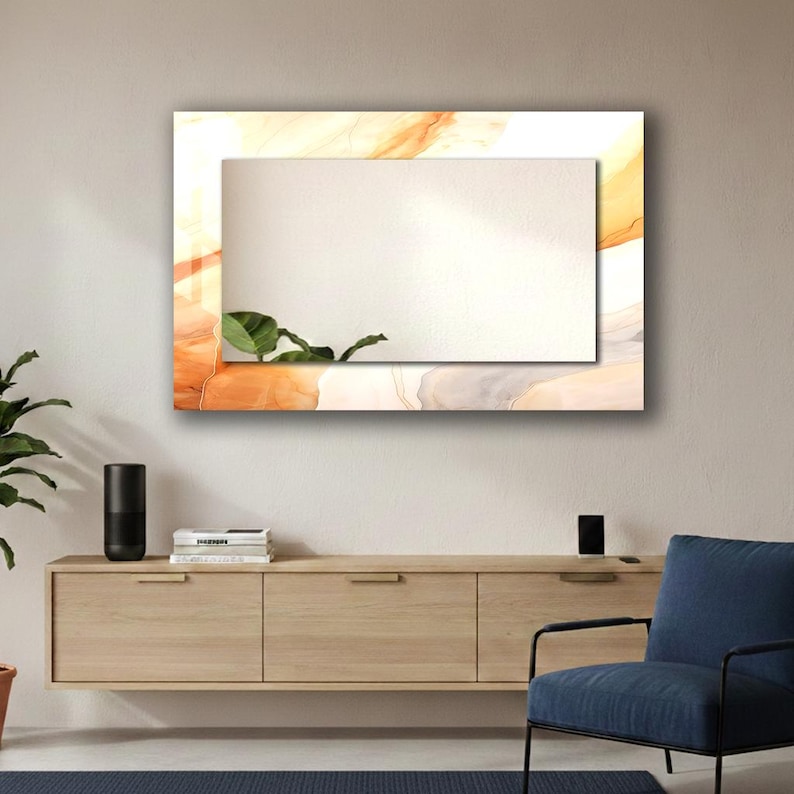 Op de afbeelding: Een rechthoekige wandspiegel met een centraal reflecterend glaspaneel omringd door een brede rand met een abstract vloeiend patroon in tinten oranje, cr&egrave;me en wit, met de reflectie van een groen plantenblad in de onderste hoek.
