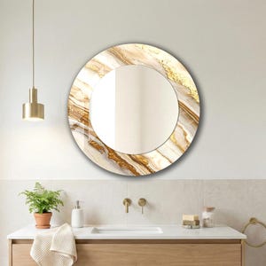 Peut inclure: Un miroir mural rond avec un motif marbr&eacute;. Le cadre pr&eacute;sente un m&eacute;lange de blanc, d'or et de brun, cr&eacute;ant une esth&eacute;tique luxueuse. Le miroir est install&eacute; au-dessus d'un meuble de salle de bain.