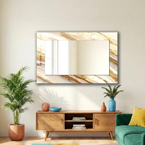 Peut inclure: Un miroir mural rectangulaire avec un cadre effet marbre aux tons dor&eacute;s et beiges. Le miroir est fix&eacute; sur un mur blanc. Un meuble en bois est en dessous. Une plante en pot est &agrave; gauche.