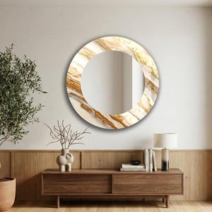 Peut inclure: Miroir rond d&eacute;coratif avec un motif marbr&eacute; blanc, beige et dor&eacute;. Le miroir est accroch&eacute; &agrave; un mur blanc au-dessus d'un meuble en bois. Le cadre pr&eacute;sente un aspect textur&eacute;. Le diam&egrave;tre du miroir est d'environ 60 cm.
