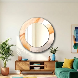 Op de afbeelding: Een ronde wandspiegel met een brede, cirkelvormige lijst versierd met een vloeiend, abstract patroon in zachte tinten oranje, beige en cr&egrave;me. Het centrale reflecterende glazen oppervlak is cirkelvormig en biedt een helder beeld.