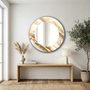 Peut inclure: Un miroir mural rond avec un motif marbr&eacute;. Le cadre pr&eacute;sente des tourbillons dor&eacute;s et beiges, cr&eacute;ant un aspect luxueux. Le miroir est accroch&eacute; sur un mur blanc au-dessus d'une console en bois.