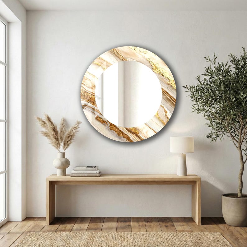 Peut inclure: Un miroir mural rond avec un motif marbr&eacute;. Le cadre pr&eacute;sente des tourbillons dor&eacute;s et beiges, cr&eacute;ant un aspect luxueux. Le miroir est accroch&eacute; sur un mur blanc au-dessus d'une console en bois.
