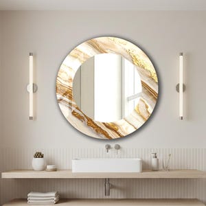 Peut inclure: Un miroir rond d&eacute;coratif avec un motif marbr&eacute; dans les tons de blanc, beige et or. Le miroir est suspendu au-dessus d'un lavabo de salle de bain. Deux lampes verticales sont mont&eacute;es sur le mur de chaque c&ocirc;t&eacute; du miroir.