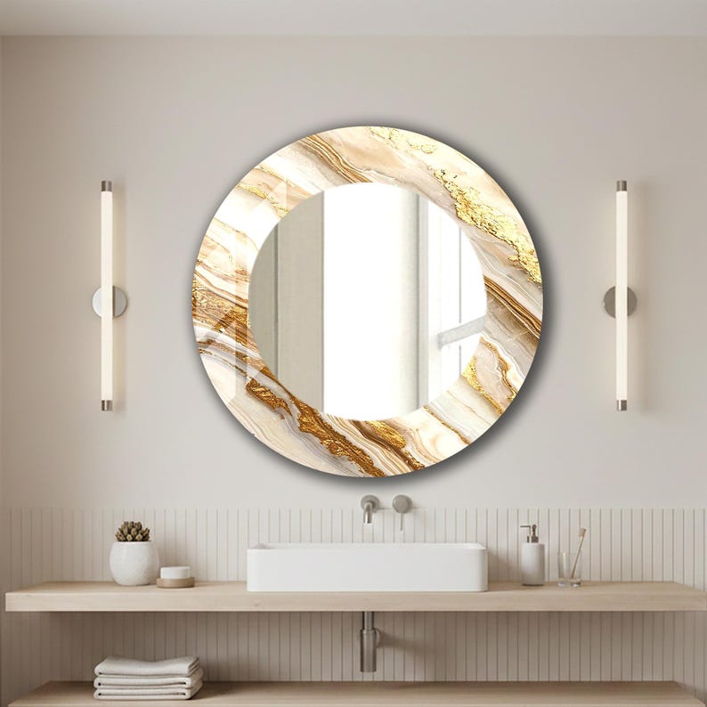 Peut inclure: Un miroir rond d&eacute;coratif avec un motif marbr&eacute; dans les tons de blanc, beige et or. Le miroir est suspendu au-dessus d'un lavabo de salle de bain. Deux lampes verticales sont mont&eacute;es sur le mur de chaque c&ocirc;t&eacute; du miroir.