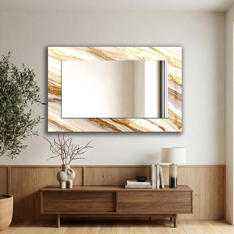 Peut inclure: Miroir mural rectangulaire avec un cadre d&eacute;coratif pr&eacute;sentant un motif semblable &agrave; du marbre dans des tons de blanc, beige et or. Le miroir est mont&eacute; sur un mur de couleur claire au-dessus d'un meuble en bois.