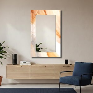 Op de afbeelding: Een rechthoekige wandspiegel met een decoratieve rand met een abstract vloeiend patroon in tinten oranje, cr&egrave;me en zachtgrijs. Het centrale reflecterende glazen oppervlak biedt een helder zicht, omlijst door het gladde bedrukte ontwerp.