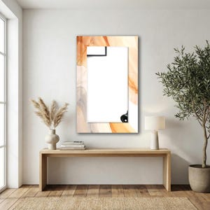 Op de afbeelding: Een rechthoekige wandspiegel met een brede lijst voorzien van een wervelend abstract patroon in tinten oranje, cr&egrave;me en lichtgrijs. De spiegel heeft een helder, reflecterend oppervlak en is verticaal aan een witte muur bevestigd.