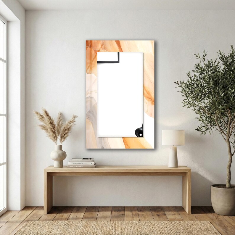 Op de afbeelding: Een rechthoekige wandspiegel met een brede lijst voorzien van een wervelend abstract patroon in tinten oranje, cr&egrave;me en lichtgrijs. De spiegel heeft een helder, reflecterend oppervlak en is verticaal aan een witte muur bevestigd.