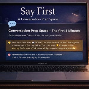 May include: A laptop screen showing the words "Say First" and "Conversation Prep Space". The screen displays information about communication for workplace leaders. A coffee cup, clock, and plant are on the desk.