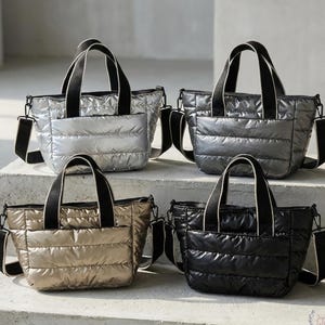 Könnte beinhalten: Vier gesteppte Tragetaschen in Silber, Grau, Gold und Schwarz werden gezeigt. Jede Tasche hat einen oberen Griff und einen abnehmbaren Schultergurt. Die Taschen bestehen aus einem glänzenden, gepolsterten Material und haben eine Vordertasche.