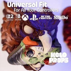 Könnte beinhalten: Ein detaillierter, mehrfarbiger Controller-Halter mit dem Text "Universal Fit For All Your Controllers". Der Halter zeigt ein stilisiertes Vogeldesign mit einer Controller-Basis. Logos für Nintendo Switch, Xbox, PlayStation und 8BitDo sind sichtbar.