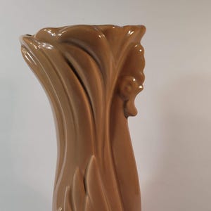 May include: A tall, brown ceramic vase with a flared top and a rounded base. The vase has a textured, fluted design that gives it a unique, artistic appearance. The vase is approximately 12 inches tall.