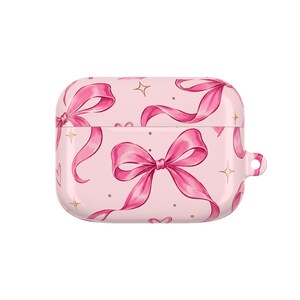 Peut inclure: Un étui de protection rose clair pour écouteurs sans fil arborant un motif répétitif de rubans et de nœuds magenta vifs, agrémenté de petites étoiles dorées à quatre branches et de minuscules points sur toute la surface de la coque.