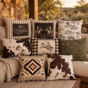 Op de afbeelding: Een collectie van acht decoratieve sierkussens met diverse western-thema ontwerpen, waaronder koeienhuidpatronen, zwart-wit gestreepte stof met afbeeldingen van cowboyhoeden en ruiters, een ruitjespatroon en een olijfgroene woestijnscène.