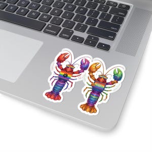 Puede incluir: Dos pegatinas de langosta coloridas con detalles de arcoíris y gafas de sol se muestran en una computadora portátil. Las langostas tienen un diseño de bandera arcoíris y están en una pose juguetona. Las pegatinas son vibrantes y llamativas.