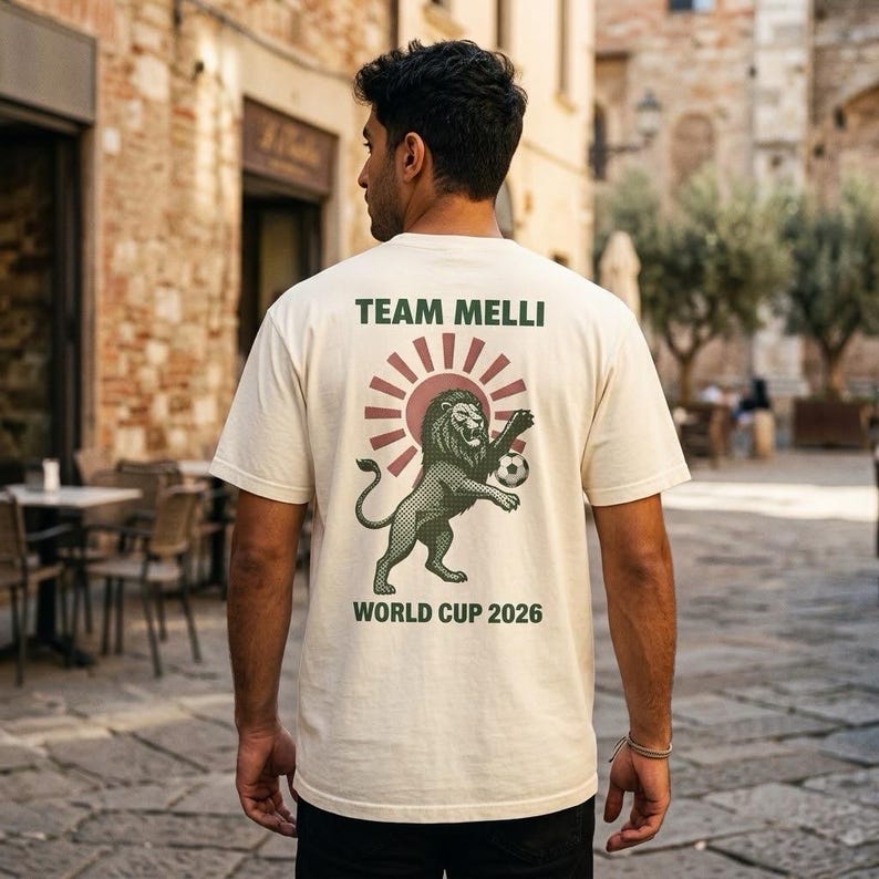 Ivory Comfort Colors heavyweight t-shirt with vintage Iran Lion and Sun World Cup 2026 badge on front chest and Team Melli vintage poster design on back, made for Iranian diaspora soccer fans.