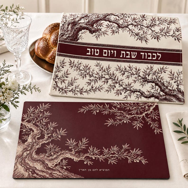May include: A rectangular challah cover in cream fabric with a dark red olive tree illustration and Hebrew text, paired with a matching dark red rectangular mat featuring a cream olive tree design and Hebrew text at the bottom edge.