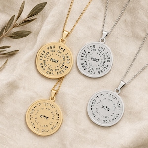 May include: Four circular pendant necklaces on thin metal chains. Two pendants are gold-toned and two are silver-toned. The pendants feature engraved text in English reading The Lord Bless You and Keep You and Hebrew text with the word Shalom.