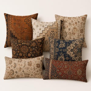 May include: A collection of six rectangular and square throw pillows featuring intricate woven patterns in shades of rust, navy blue, cream, and dark brown. The designs include geometric borders and floral motifs reminiscent of traditional rug patterns.