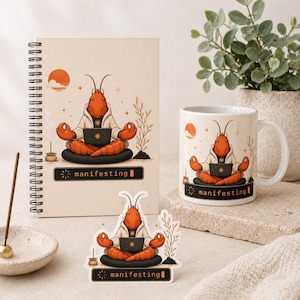 May include: A spiral-bound notebook, a white mug, and a sticker featuring a cartoon lobster meditating with a laptop. The design includes the text "manifesting" and a sun graphic. The items are beige and white.